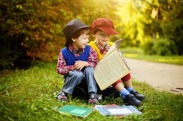 Chłopcy siedzą na trawie i wspólnie czytają książkę