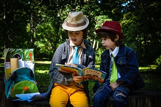 Chłopcy siedzą w cieniu drzewa i przeglądają podręcznik szkolny