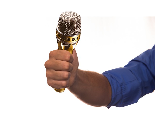 Mikrofon trzymany przez męską rękę.